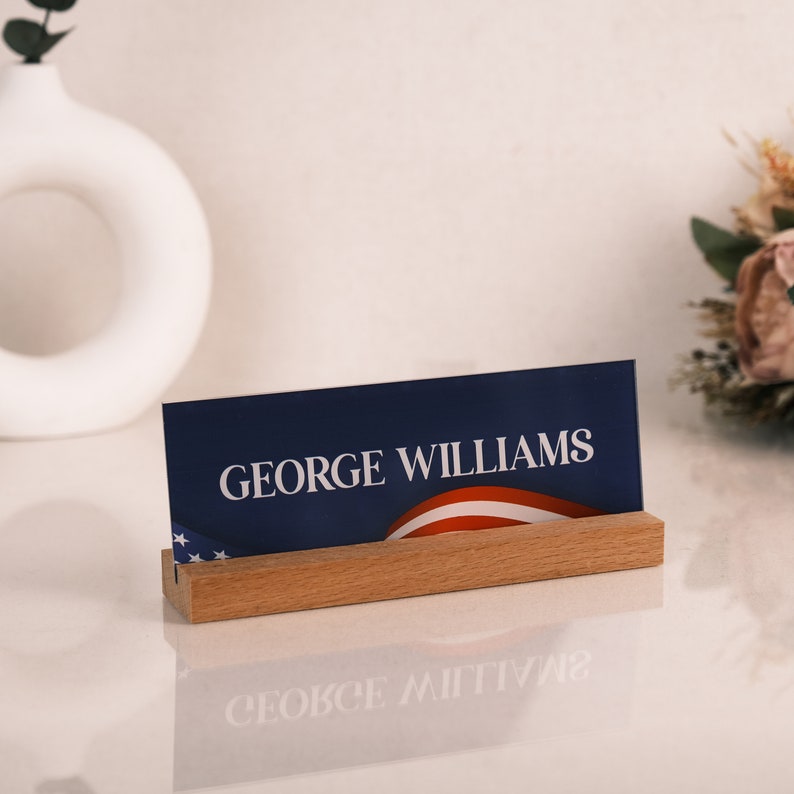 May include: A wooden name card holder with a blue and red card that says "GEORGE WILLIAMS".