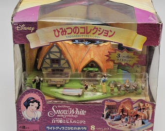 Può includere: Un playset Disney di Biancaneve e i Sette Nani nella sua confezione originale. La scatola presenta una finestra trasparente che mostra un cottage in miniatura, statuette di Biancaneve e dei nani e altre scene. La scatola ha testo giapponese e il logo Disney.
