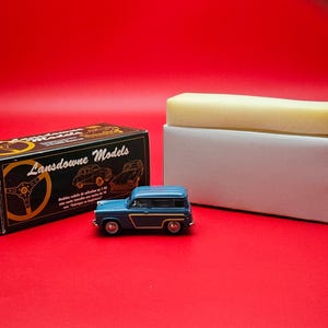 May include: A blue and gold Lansdowne Models die-cast model car, with a matching box and a white box with a yellow foam insert, set against a red background. The model car is a vintage station wagon.
