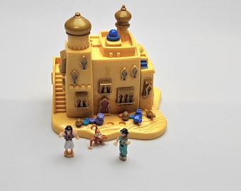 Può includere: Un castello giocattolo di plastica gialla con due cupole color oro e un accento blu. Il castello ha una scala e diverse finestre. Tre piccole statuette e altri accessori sono di fronte al castello.