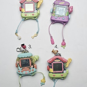 Könnte beinhalten: Vier bunte, vintage LPS (Littlest Pet Shop) elektronische Haustierspielzeuge. Jedes Spielzeug hat ein hausförmiges Design mit einem Bildschirm, einer Schnur und dekorativen Anhängern. Die Spielzeuge sind in verschiedenen Farben erhältlich, darunter Rosa, Grün, Blau und Lila.