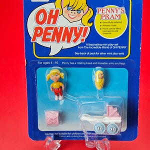 May include: A vintage Bluebird "Oh Penny!" mini play-set, featuring a doll, a baby, a pink pram, and accessories. The packaging includes text about the features and age range. The pram's wheels rotate.