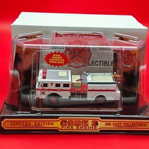 Peut inclure: Un modèle réduit de camion de pompiers Code 3, blanc et rouge, présenté dans un boîtier en plastique transparent. Le modèle porte le numéro 7 et des marquages de pompiers. L'emballage indique "Édition Limitée" et "Objet de collection moulé sous pression."