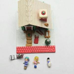 Może przedstawiać: Miniaturowy zestaw do zabawy o tematyce bożonarodzeniowej z domkiem, akcesoriami i figurkami. Domek ma beżowy dach, czerwoną ceglaną podstawę oraz zielony i czerwony guzik. Zawiera bałwana, dwoje dzieci i sanie zaprzężone w konie.