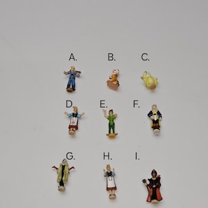 Op de afbeelding: Negen kleine plastic figuurtjes van personages uit Disney-films. De figuurtjes zijn van A tot en met I gelabeld. De personages zijn Peter Pan, Captain Hook, Shere Khan, een gele vogel, een vrouw in een blauwe jurk, een vrouw in een rode jurk, een vrouw in een groene jurk, een vrouw in een bruine jurk en een man in een zwarte mantel.