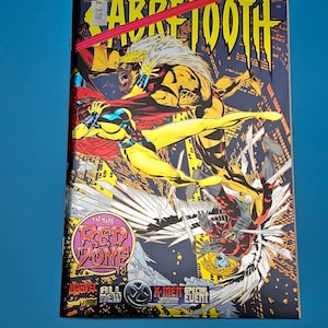 May include: A comic book titled "Sabretooth" with action-packed illustrations. The cover features a yellow and black figure in combat, with the text "IN THE RED ZONE" and "X-MEN SPECIAL EVENT" visible.
