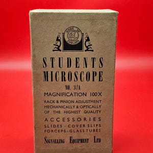 Könnte beinhalten: Vintage Kartonbox für ein Studentenmikroskop mit der Aufschrift "STUDENTS MICROSCOPE" und "MADE IN ENGLAND". Die Box enthält Zubehör und Spezifikationen, einschließlich einer 100-fachen Vergrößerung.