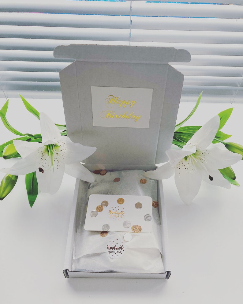 May include: A white gift box with a gold inscription that reads "Happy Birthday". The box is open and contains a white card with gold confetti and the text "Handmade with Love".