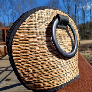 Peut inclure: Un sac &agrave; main en paille tress&eacute;e avec une poign&eacute;e en cuir noir. Le sac a une forme arrondie et une bordure noire.