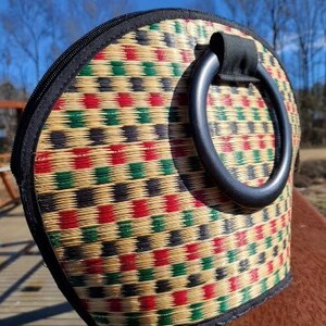 Peut inclure: Un sac &agrave; main tiss&eacute; avec une poign&eacute;e noire et un motif g&eacute;om&eacute;trique color&eacute; de carr&eacute;s rouges, verts et noirs sur un fond beige.
