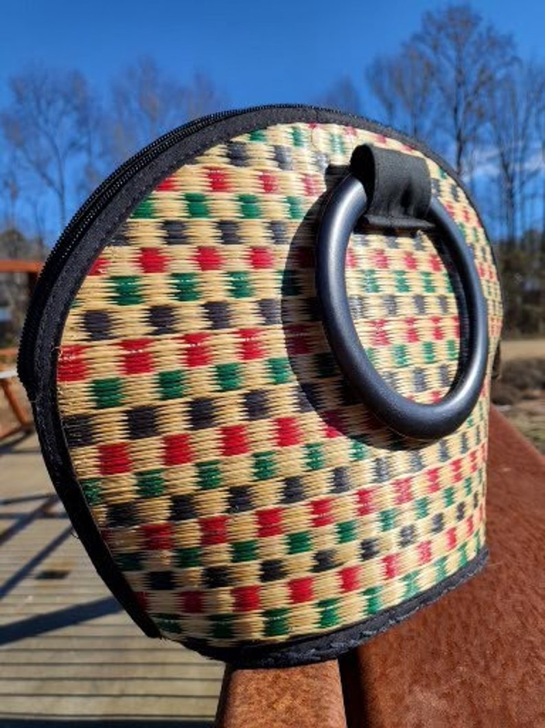 Peut inclure: Un sac &agrave; main tiss&eacute; avec une poign&eacute;e noire et un motif g&eacute;om&eacute;trique color&eacute; de carr&eacute;s rouges, verts et noirs sur un fond beige.