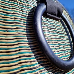 Peut inclure: Un sac tiss&eacute; avec une poign&eacute;e noire. Le sac est fait de mat&eacute;riaux naturels et pr&eacute;sente un motif ray&eacute; dans les tons de vert, marron et beige.