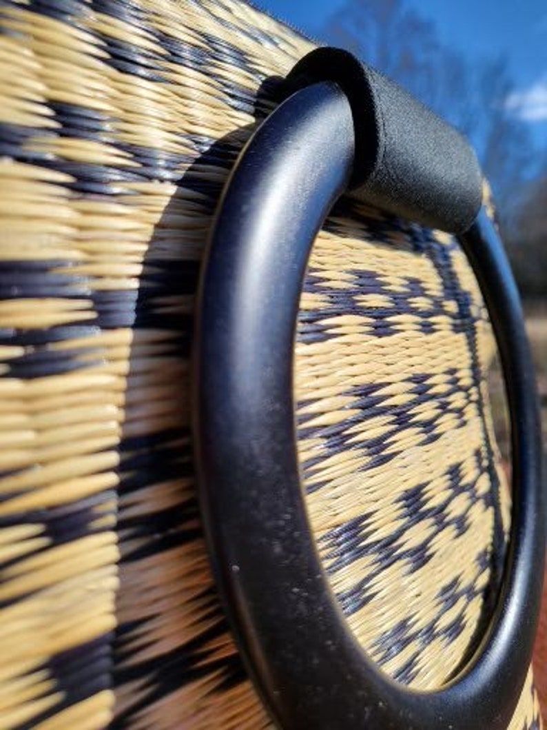 Peut inclure: Gros plan sur une poign&eacute;e tiss&eacute;e noire sur un sac en paille. La poign&eacute;e est faite d'un mat&eacute;riau noir &eacute;pais et a une surface lisse et arrondie.