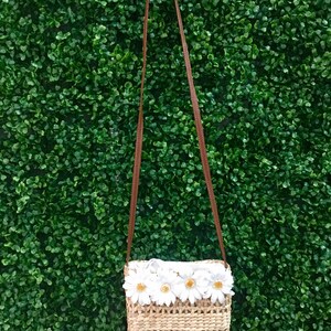 May include: A small woven straw bag with a brown strap and white daisy flower embellishments.