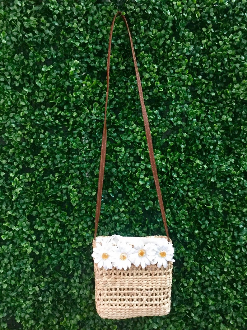 May include: A small woven straw bag with a brown strap and white daisy flower embellishments.