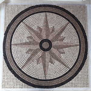 Peut inclure: Une mosaïque représentant une rose des vents. Le motif est composé de petits carreaux carrés beiges, bruns et noirs. La rose des vents est centrée dans un cercle, créant un élément décoratif pour l'intérieur.