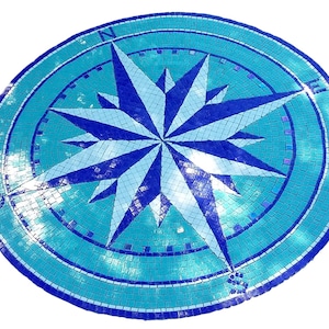 Op de afbeelding: Een blauwe en witte mozaïek kompasroos ontwerp. De kompasroos is gemaakt van kleine, vierkante tegels en is geplaatst in een cirkelvormig frame.