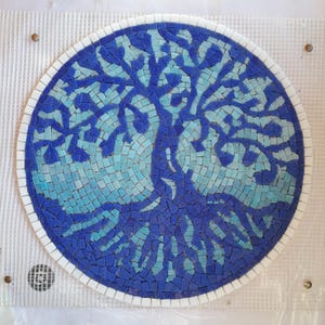 Może przedstawiać: Okrągła mozaika przedstawiająca drzewo. Drzewo jest w odcieniach niebieskiego i turkusowego, na ciemnoniebieskim tle. Mozaika jest obramowana białą obwódką, tworząc kontrast. Dzieło sztuki znajduje się na białym podłożu z siatki.
