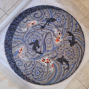 May include: Circular mosaic art piece featuring koi fish and abstract shapes in shades of blue, gray, white, and orange. The mosaic is made of small, square tiles and has a detailed, artistic design. The artwork is likely for home decor.