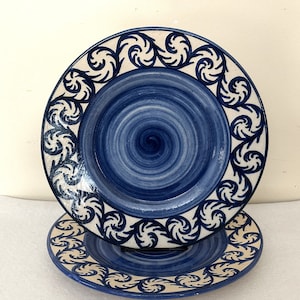 May include: Two blue and white ceramic plates with a swirling design and a blue and white floral border.