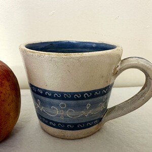 May include: A white ceramic mug with a blue band and white cursive writing that says "Jicki".