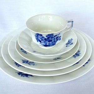 May include: A set of five white porcelain plates with blue floral designs. The plates are stacked on top of each other, with a matching teacup and saucer on top.