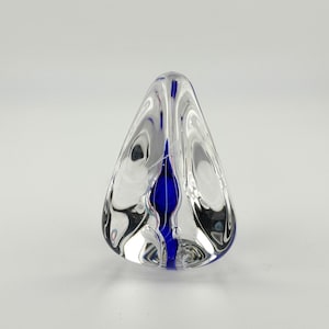 May include: A clear glass paperweight with a blue swirl inside. The paperweight is shaped like a cone.