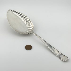 May include: A silver serving spoon with a scalloped edge and a beaded handle. The spoon is about 10 inches long.
