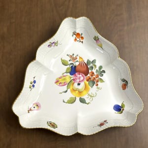 May include: White porcelain serving dish with a scalloped edge and gold trim. The dish features a central floral and fruit design with pears, apples, and berries in shades of red, yellow, blue, and orange. The dish is approximately 10 inches in diameter.