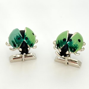 May include: A pair of silver cufflinks with green and black enamel ladybug designs.