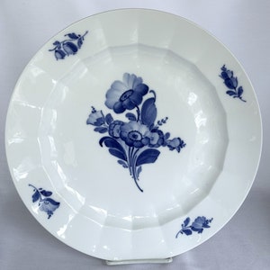 May include: A white porcelain dinner plate with a blue floral design. The plate has a scalloped edge and a raised centre.