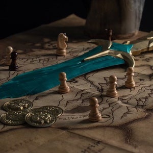 May include: A teal and gold sword lies on a brown map with chess pieces scattered around it. There are also gold coins on the map.