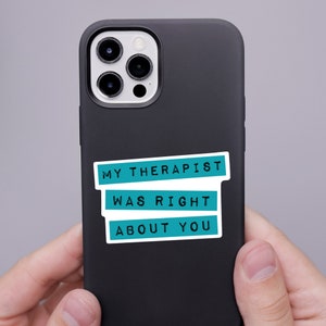 May include: A matte black smartphone case featuring a rectangular sticker with three teal horizontal bars. The text in black capital letters reads MY THERAPIST WAS RIGHT ABOUT YOU, with each line of text contained within its own teal bar.