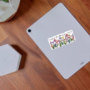 K&ouml;nnte beinhalten: Ein rechteckiger Aufkleber mit einem bunten Wildblumen-Design und dem Text "Seht die Lilien, wie sie wachsen. Lukas 12,27". Er zeigt Blumen in Rosa, Lila, Gelb und Gr&uuml;n.