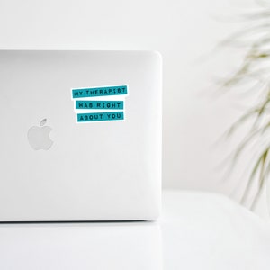 May include: A rectangular sticker with a teal background and black text that reads MY THERAPIST WAS RIGHT ABOUT YOU, applied to the lid of a silver laptop. The sticker features three separate lines of text, each on its own teal horizontal bar.