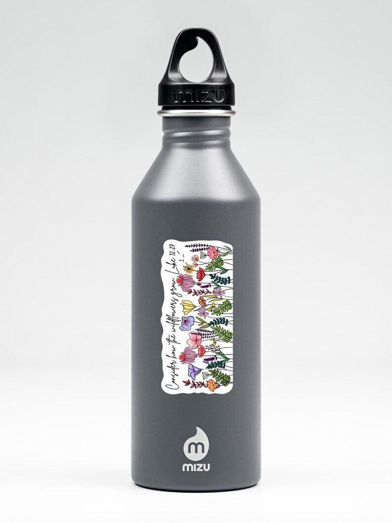 K&ouml;nnte beinhalten: Eine graue Mizu-Trinkflasche mit schwarzem Deckel. Ein Aufkleber auf der Flasche zeigt eine farbenfrohe Illustration von Wildblumen und den Text "Betrachtet die Lilien... Lukas 12,27."