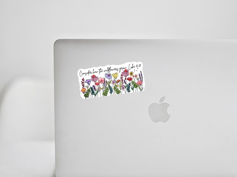 K&ouml;nnte beinhalten: Ein Aufkleber mit einer Aquarellillustration von bunten Wildblumen. Der Aufkleber hat den Text "Betrachtet die Lilien, wie sie wachsen. Lukas 12,27" in handschriftlicher Schrift. Der Aufkleber ist rechteckig mit wei&szlig;em Hintergrund.