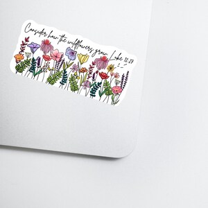 K&ouml;nnte beinhalten: Ein Aufkleber mit einer bunten Wildblumenillustration und dem Text "Consider how the wildflowers grow. Luke 12:27." Das Design zeigt verschiedene Blumen in Rosa, Lila, Gelb und Orange, mit gr&uuml;nen Bl&auml;ttern.