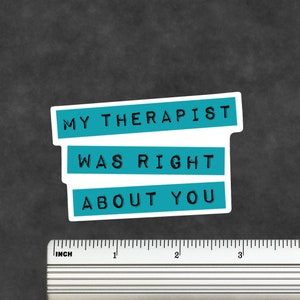 May include: A rectangular sticker with a white border featuring three teal horizontal bars, each containing black text that reads MY THERAPIST WAS RIGHT ABOUT YOU. A metal ruler is positioned below the sticker, showing it is approximately 7.6 cm wide.
