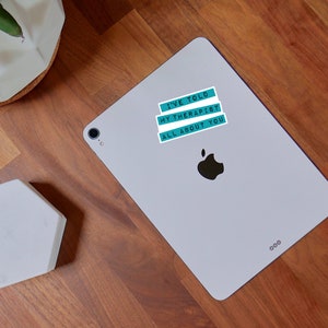 May include: A silver tablet featuring a rectangular sticker with three teal horizontal bars. The text on the sticker reads I'VE TOLD MY THERAPIST ALL ABOUT YOU in black capital letters. The tablet has a black Apple logo centred on the back surface.