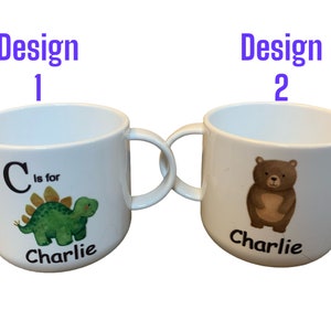 Op de afbeelding: Twee witte keramische bekers met handvatten. De beker links heeft een groene dinosaurus met de letter C en de tekst "C is for Charlie". De beker rechts heeft een bruine beer met de tekst "Charlie".
