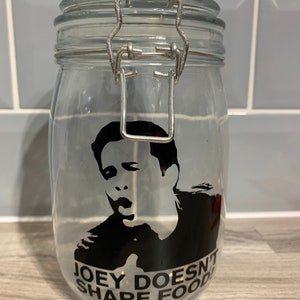 May include: A clear glass jar with a metal clasp lid. The jar has a black and white sticker with a picture of Joey from the TV show Friends and the text "Joey Doesn't Share Food".