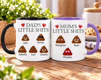May include: Two white ceramic mugs with colored handles and interiors. The left mug has a black handle and features the text DAD'S LITTLE SHITS with five brown poop emojis labeled Jack, Simon, Isabelle, Carl, and Charlie. The right mug has a purple handle and features the text MUM'S LITTLE SHITS with three poop emojis labeled Maeghan, Ryan, and Phoebe.
