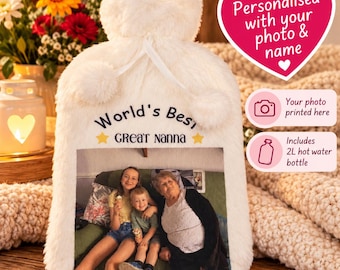 Op de afbeelding: Een witte kunstbont warmwaterkruikhoes met een afgedrukte foto van een jong persoon, een kind en een ouder persoon op een bank. De tekst luidt World's Best GREAT NANNA met twee gele sterren. Inclusief een warmwaterkruik van 2 liter.