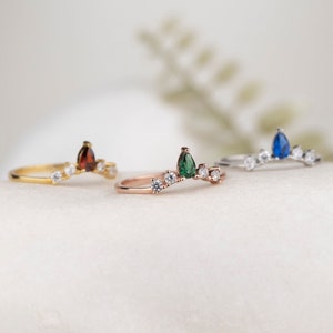 May include: Three delicate rings with a pear-shaped gemstone and small round stones. The rings are in gold, rose gold, and silver with green, red, and blue gemstones.
