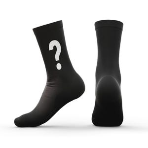 Può includere: Due calzini neri, uno angolato, l'altro dritto. Il calzino angolato presenta un grande punto interrogativo bianco sul lato. I calzini sono realizzati in un materiale morbido, probabilmente a maglia, e sono progettati per l'uso quotidiano.