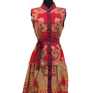 May include: A red sleeveless dress with a floral pattern and a maroon button-up front. The dress has a maroon sash tied at the waist.