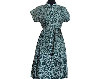 Puede incluir: Un vestido midi estampado en verde y blanco con botones en la parte delantera y un cinturón. El vestido tiene mangas cortas y una falda ligeramente acampanada.