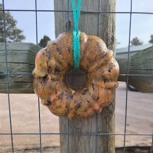 Puede incluir: Un lamiendo de sal de color marrón y naranja con forma de rosquilla que cuelga de un poste de madera de una valla con una cuerda azul.