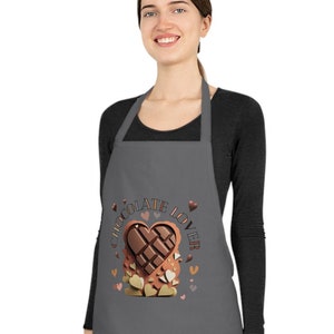 May include: A grey apron featuring a heart-shaped chocolate design and the words "Chocolate Lover." The design includes a chocolate bar, hearts, and other chocolate pieces. The apron is worn by a person.